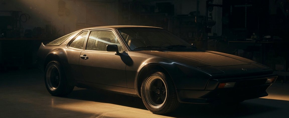 1980s German wedge-profile sports coupé lit by a raking beam in a darkened workshop